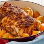 A close up of a roast pork loin with butternut squash and apples in a roasting pan.