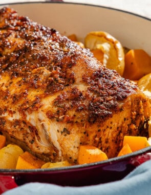 A close up of a roast pork loin with butternut squash and apples in a roasting pan.