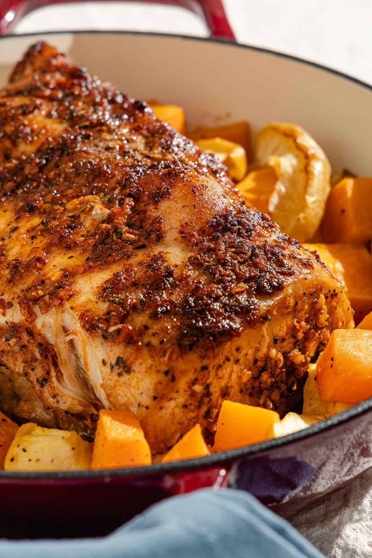 A close up of a roast pork loin with butternut squash and apples in a roasting pan.