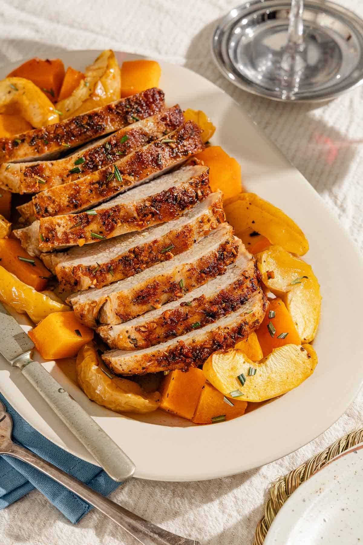 A close up of sliced roast pork loin with butternut squash and apples on a serving platter with a knife.