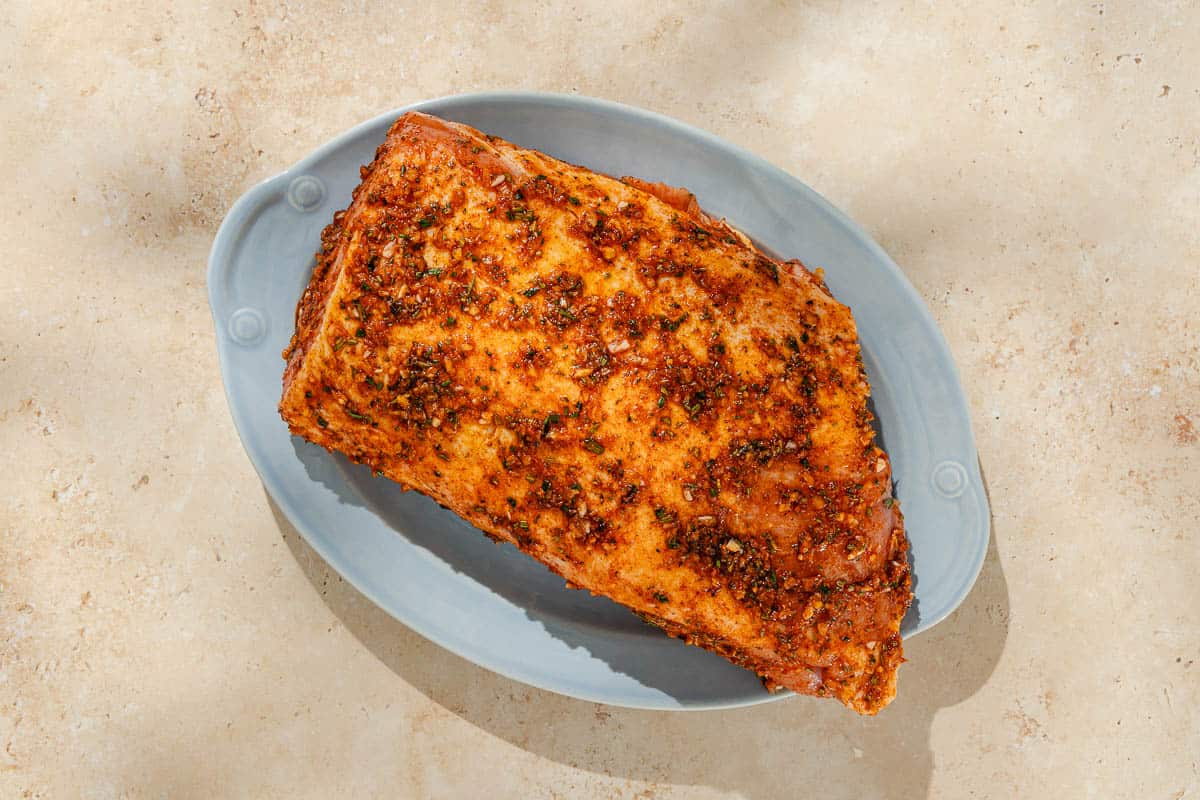 An overhead photo of an uncooked pork loin rubbed in seasonings on a platter.