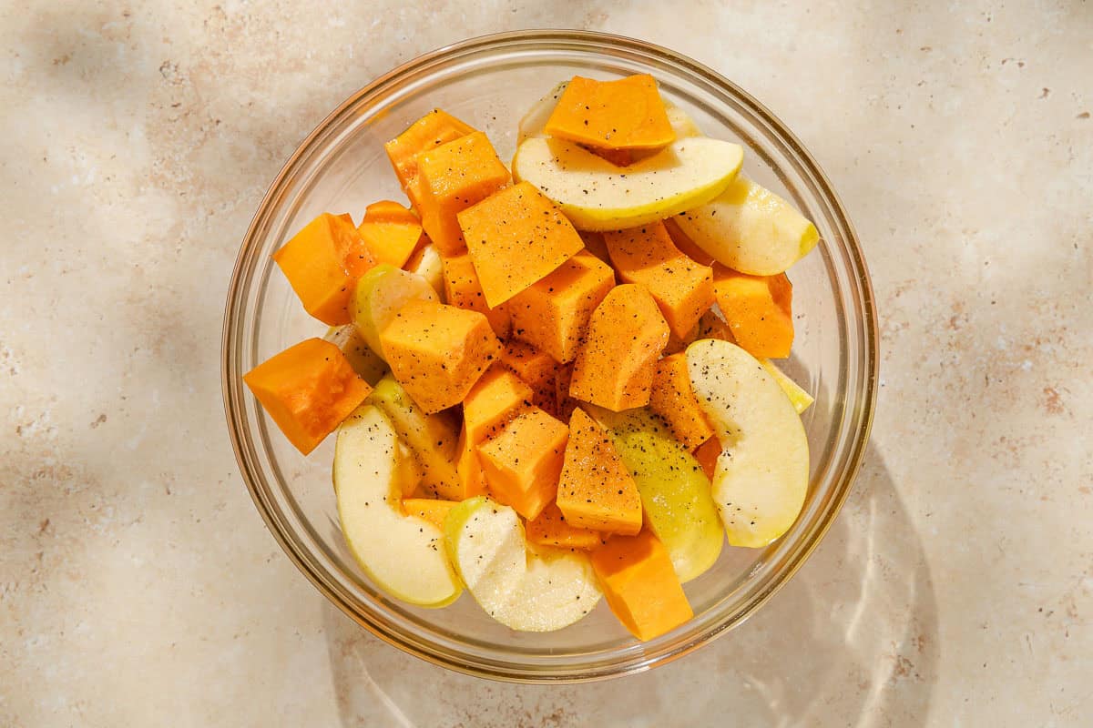 Cubed butternut squash and apple slices seasoned with salt and pepper in a bowl.