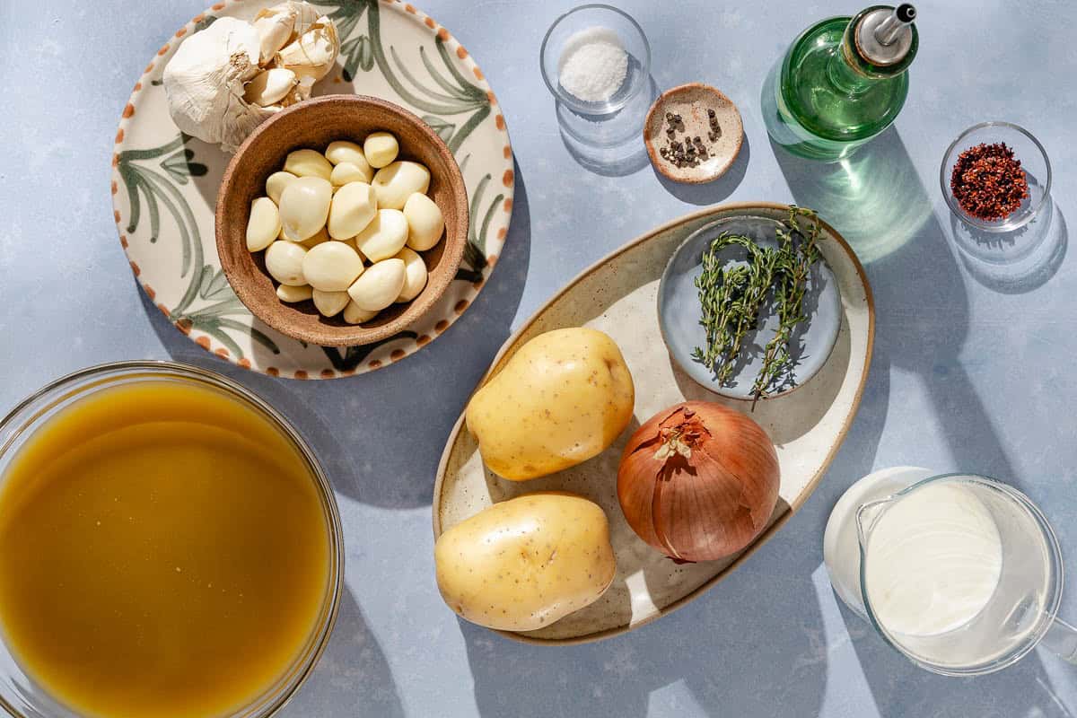 Ingredients for garlic soup including garlic, olive oil, aleppo pepper, onion, potatoes, stock, thyme, salt, and milk.