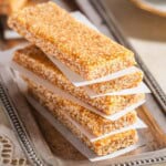 A stack of 5 pieces of greek sesame candy on a silver tray, each on separated by a piece of parchment paper.