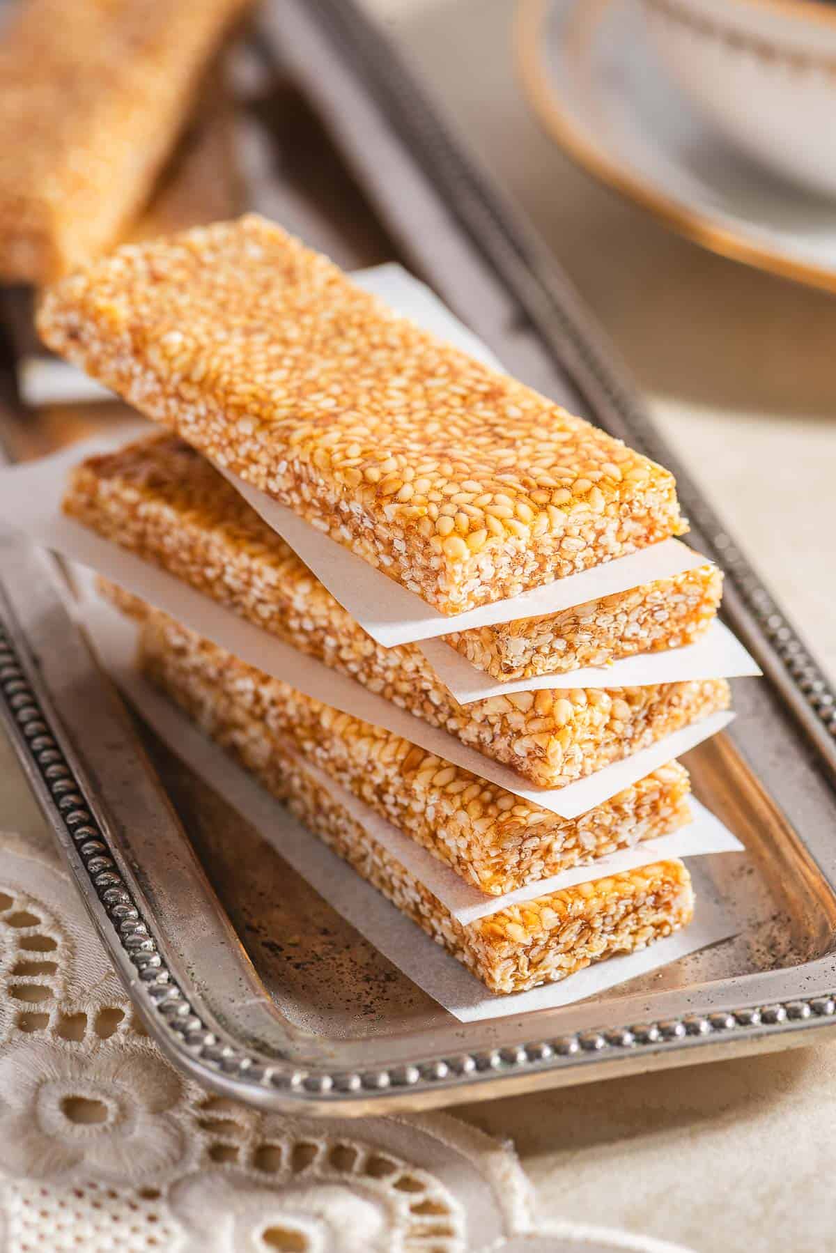 A stack of 5 pieces of greek sesame candy on a silver tray, each on separated by a piece of parchment paper.