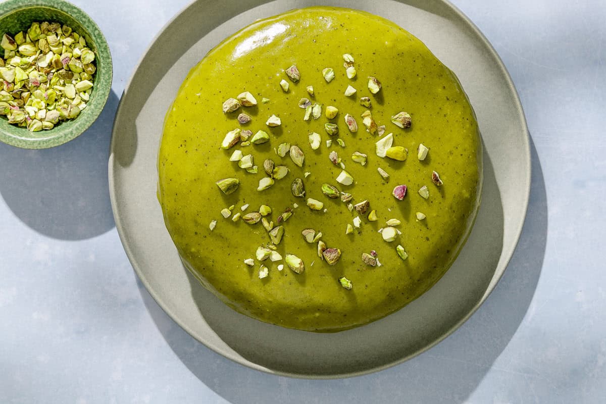 An overhead photo of the pistachio cake on a platter next to a bowl of pistachios.