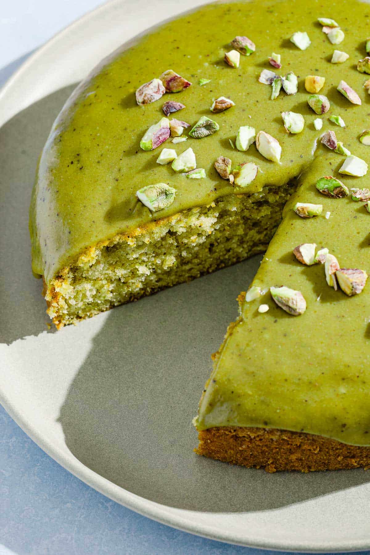 A close up of the pistachio cake with one piece removed on a platter.