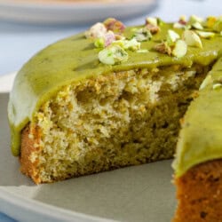 A close up of the pistachio cake with one piece removed on a platter.