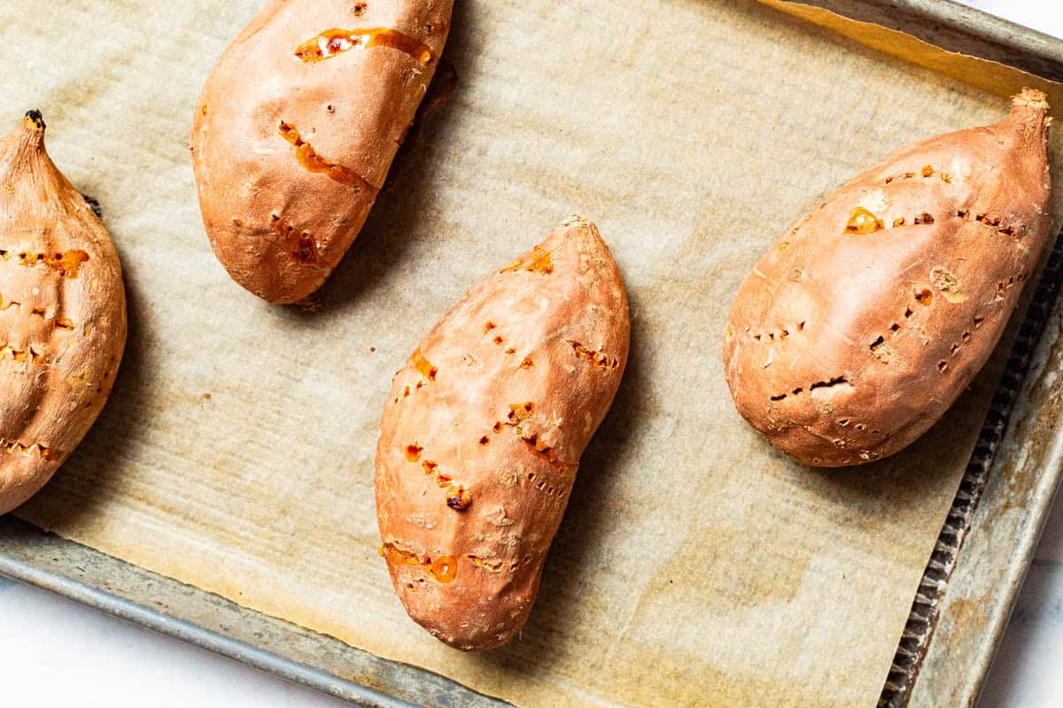 An overhead photo of 4 roasted sweet potatoes on a parchment lined sheet pan.