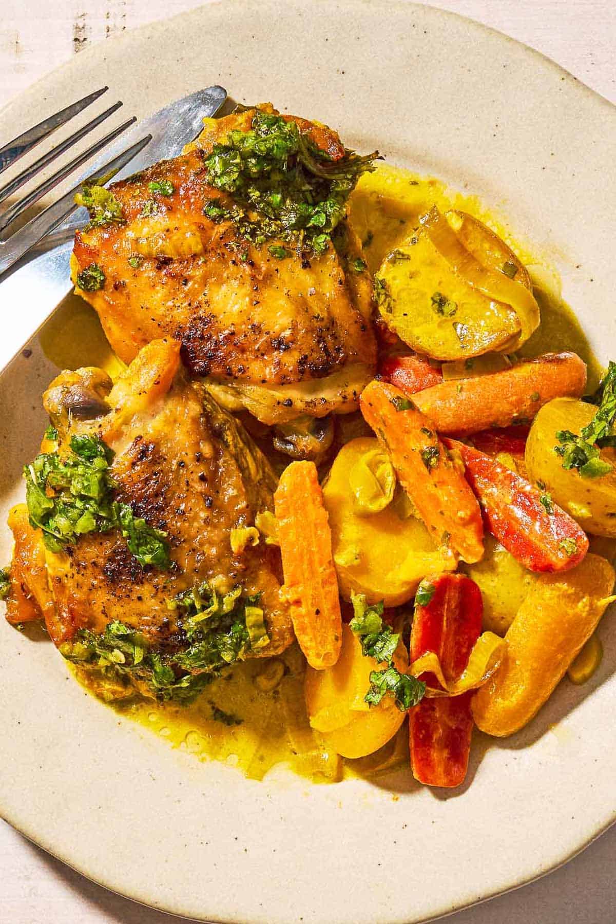 An overhead photo of a serving of creamy saffron chicken with mascarpone and lemony cilantro dressing on a plate with a knife and fork.