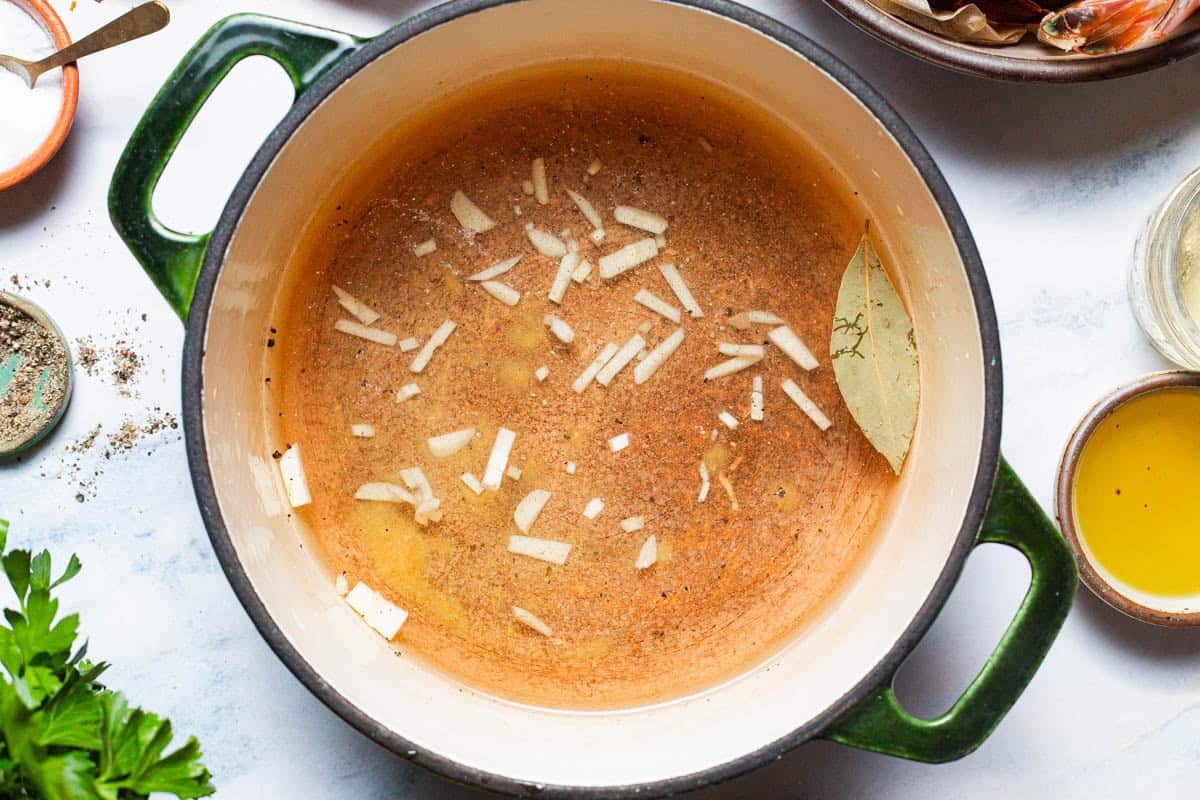 An overhead photo of the lobster broth in a large pot, before the lobster is added. Surrounding this are various other ingredients for the stew.