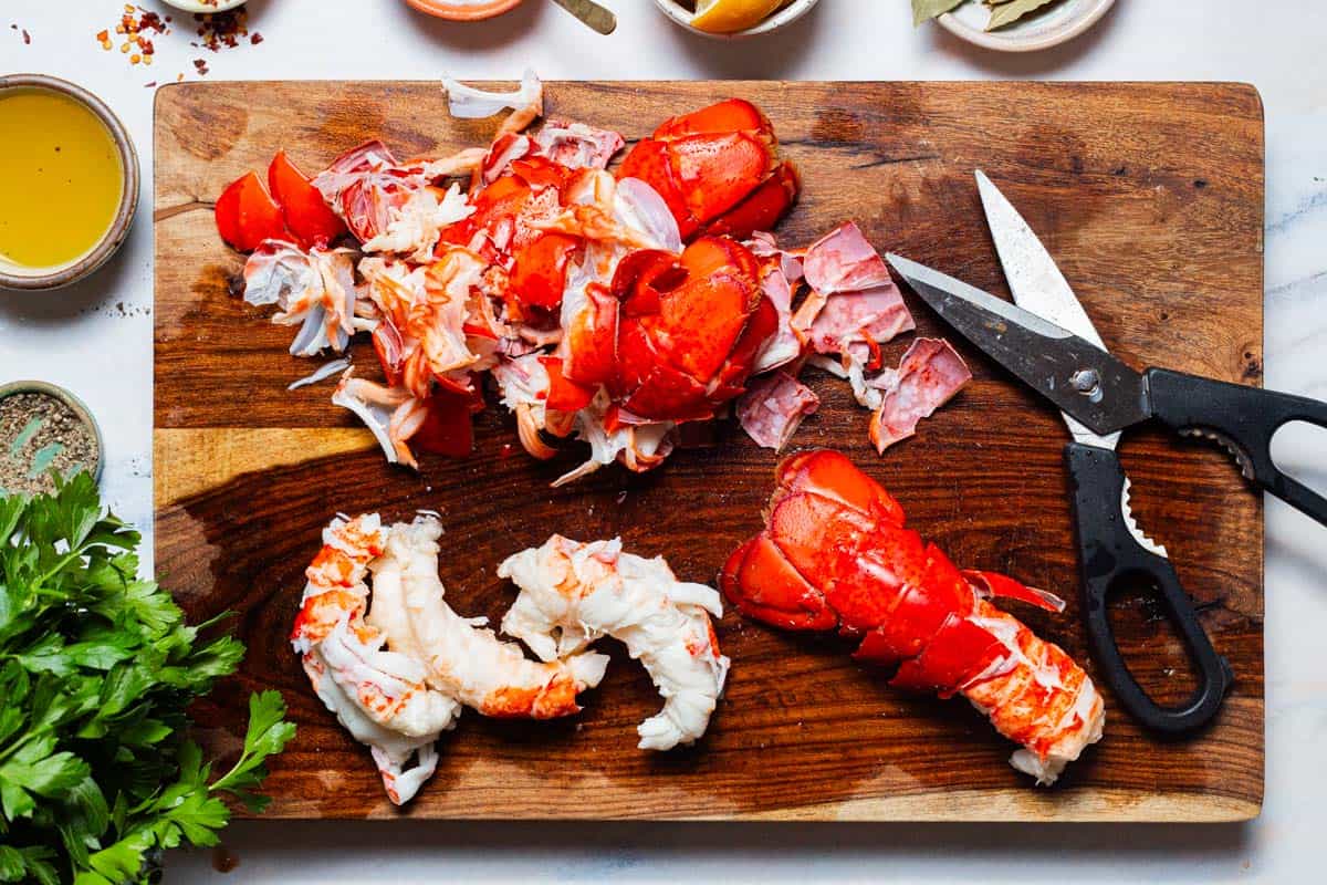 An overhead photo of the lobster meat after being removed from it's shells on a cutting board with a pair of scissors. Surrounding this are the various other ingredients for the stew.