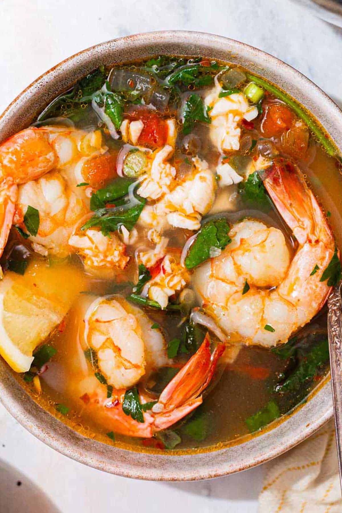 A close up of a bowl of seafood stew with a spoon.