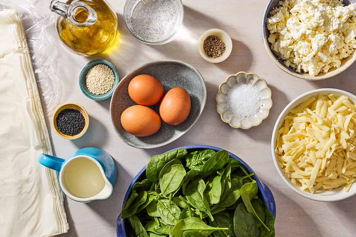 Ingredients for Turkish Borek including phyllo dough, olive oil, eggs, white and black sesame seeds, spinach, salt, black pepper, cheddar and feta cheeses, milk, and sparkling water.