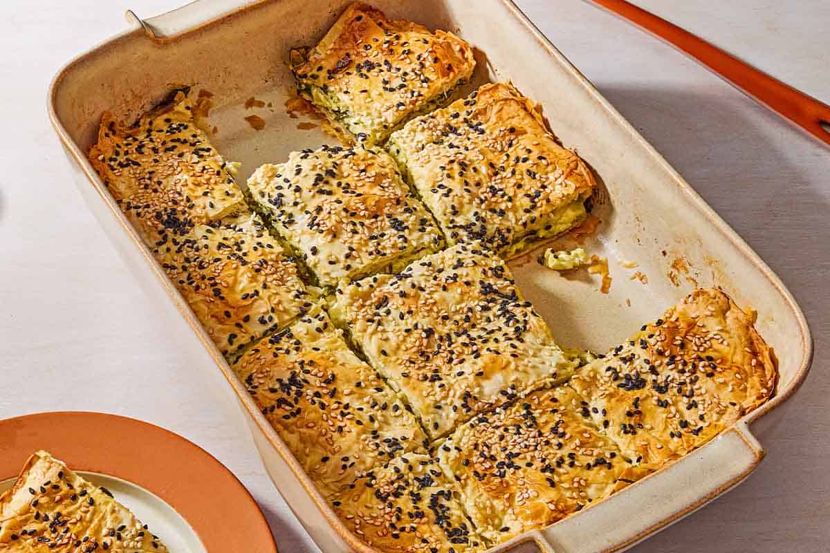 Sliced turkish borek in a baking dish with a few pieces removed. Next to this a piece of the borek on a plate.