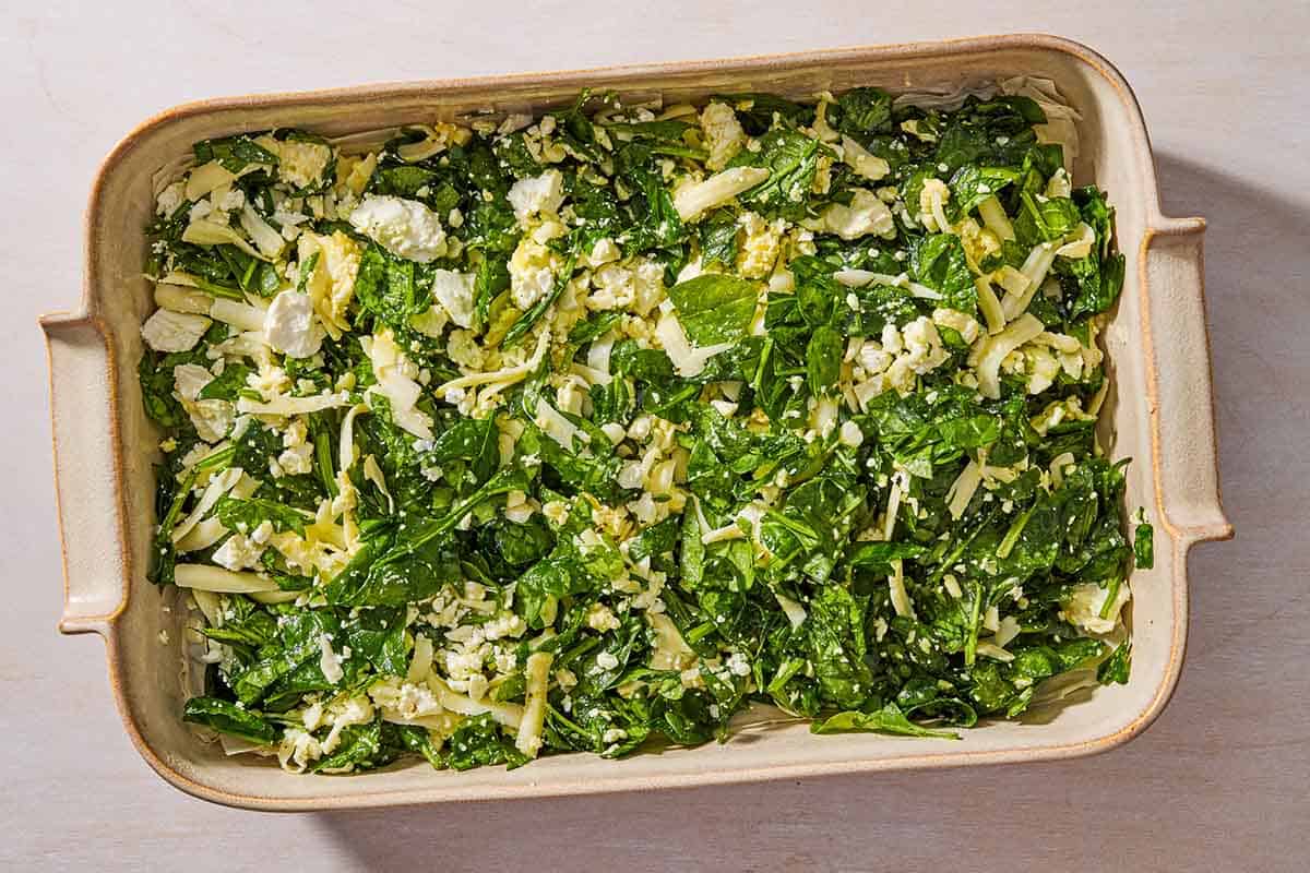 An overhead photo of the filling for the borek spread evenly over the first layer of phyllo dough in a baking dish.