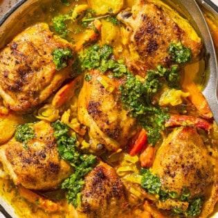 A close up of creamy saffron chicken with mascarpone and lemony cilantro dressing in a skillet with a serving spoon.