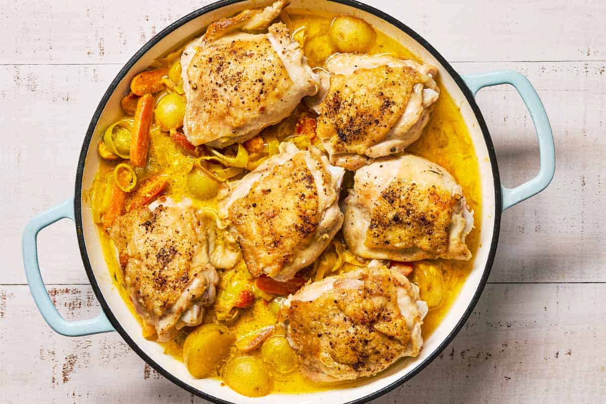 The browned chicken thighs placed on the vegetables in the creamy sauce in a skillet.