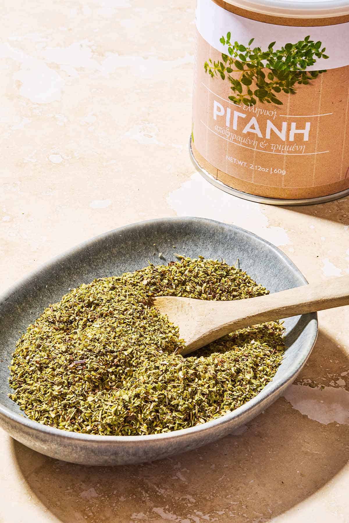 Dried oregano in a bowl with a wooden spoon. In the background is a canister.