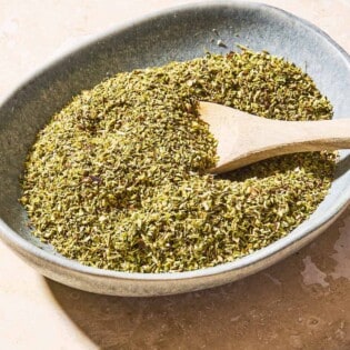 Dried oregano in a bowl with a wooden spoon.