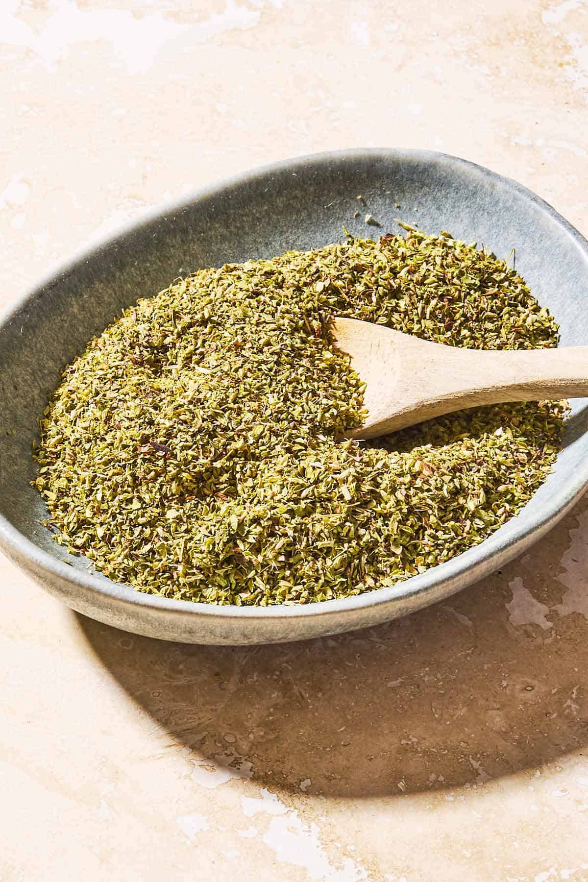 Dried oregano in a bowl with a wooden spoon.