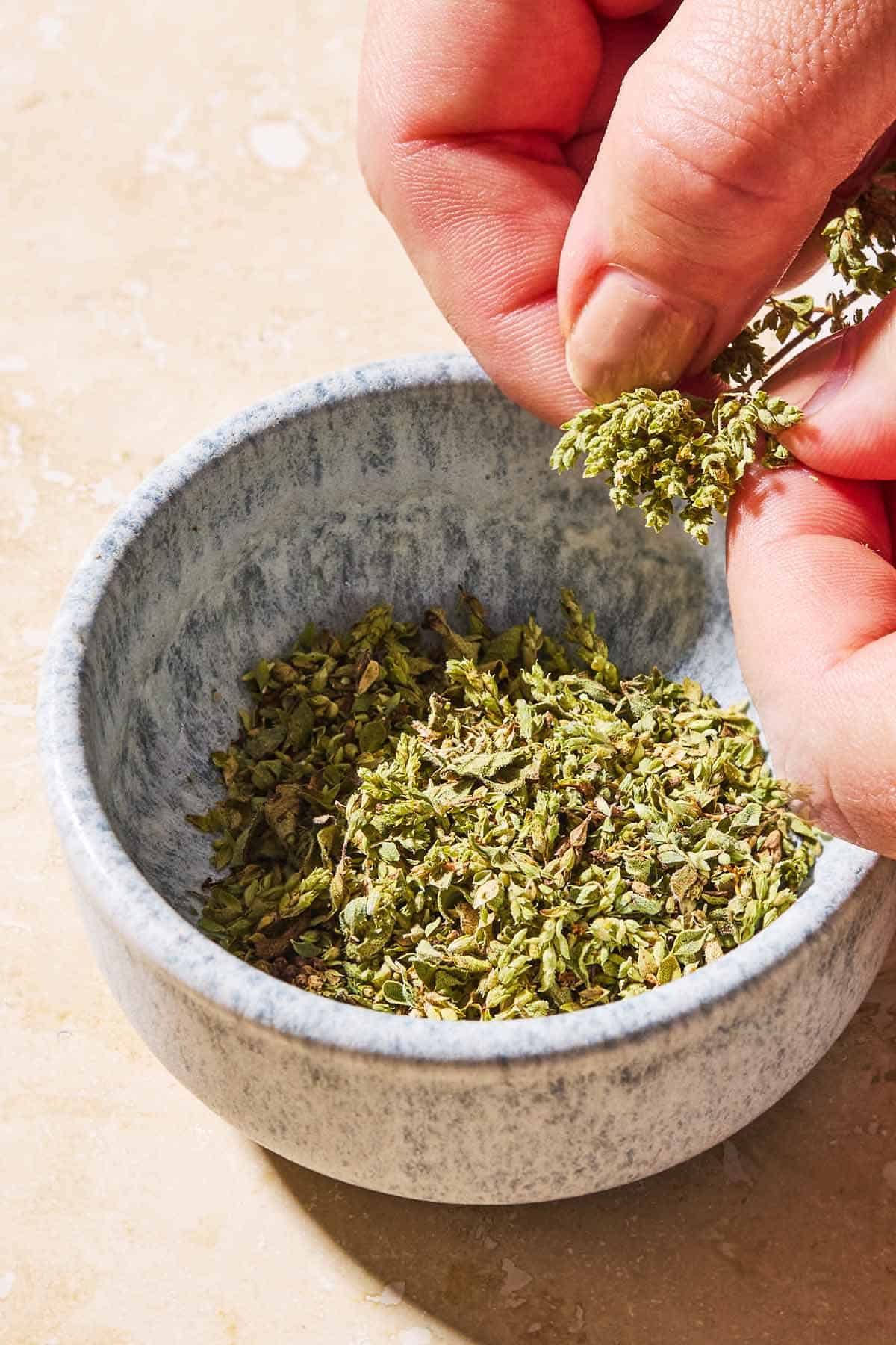 Dried oregano being pulled from the stem over a bowl.