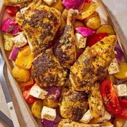 An overhead photo of oven roasted whole chicken and potatoes along with other vegetables and cubed feta on a platter.