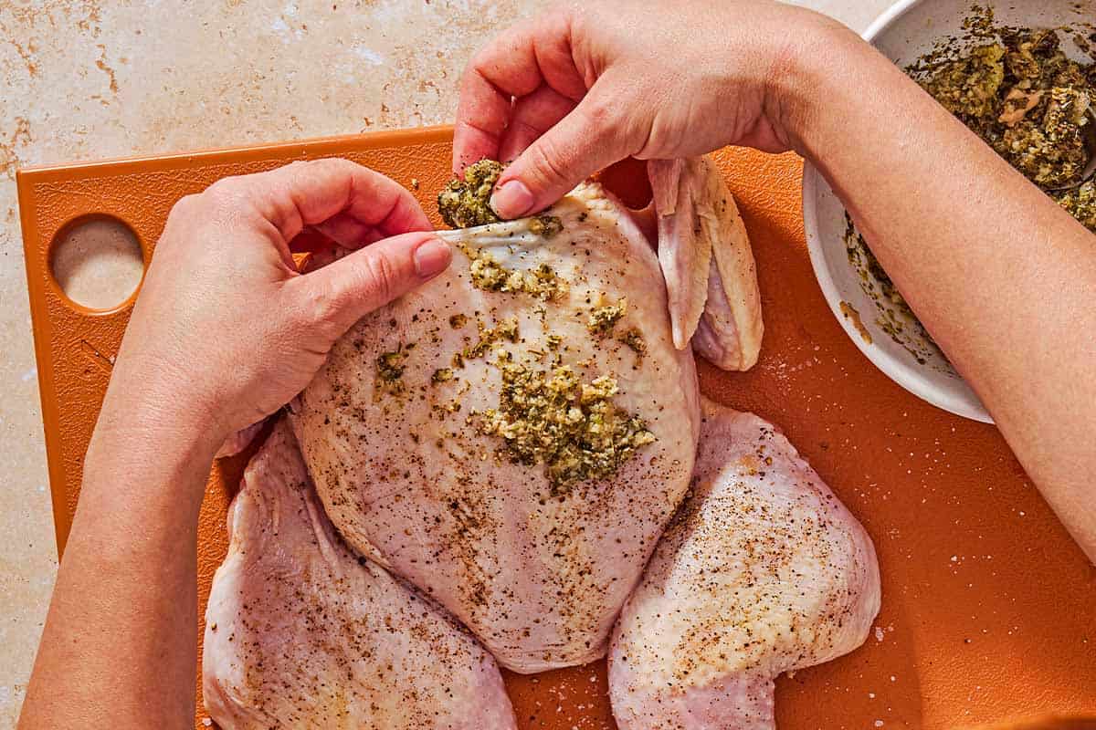 An overhead photo of the garlic lemon rub being rubbed all over the chicken and under the skin. Next to this is a bowl of the rub.