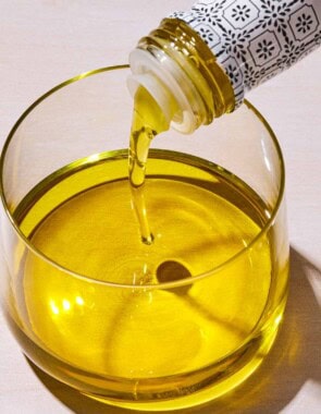 Olive oil being poured from a bottle into a glass bowl.