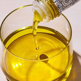 Olive oil being poured from a bottle into a glass bowl.