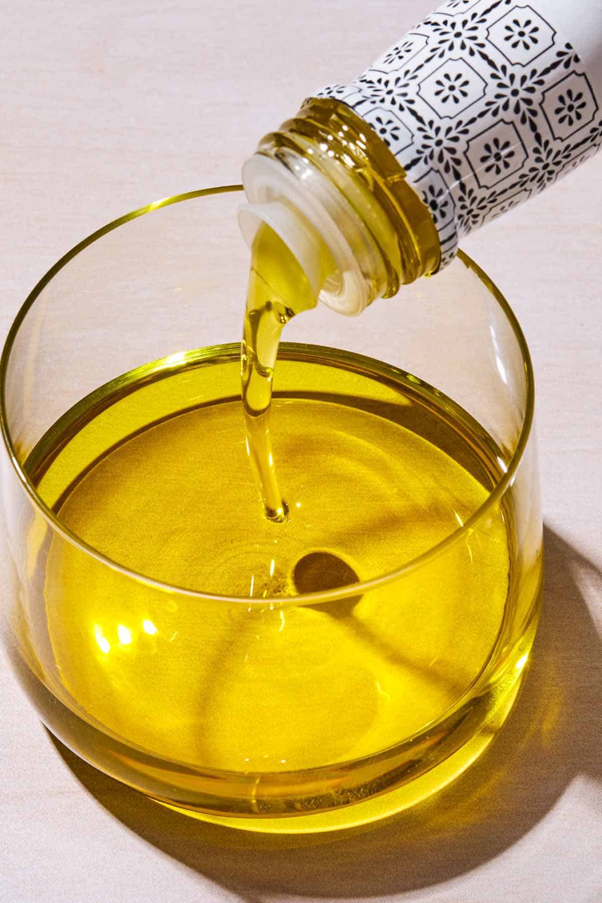 Olive oil being poured from a bottle into a glass bowl.