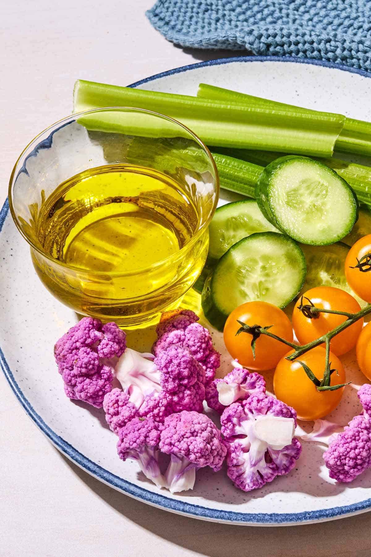 A close up of a plate of various raw vegetables along with a glass bowl filled with olive oil.