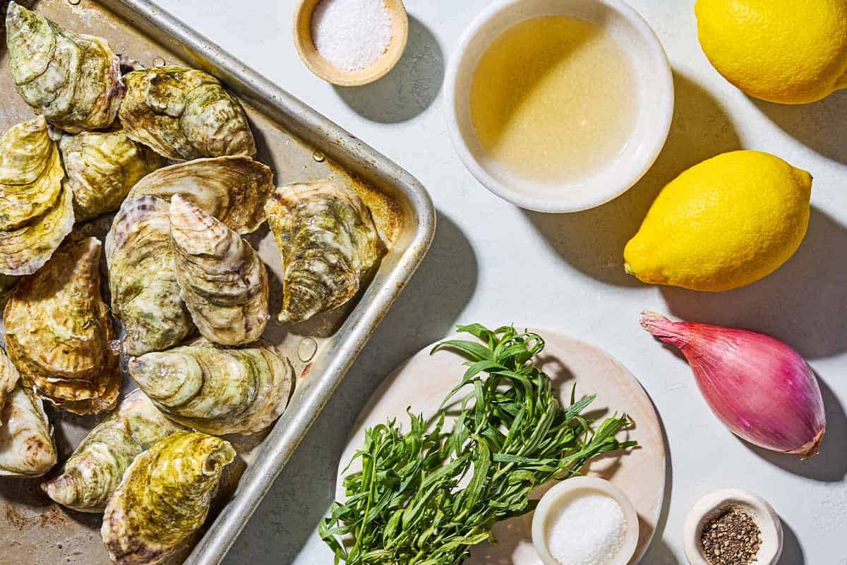 Ingredients for raw oysters with mignonette sauce including raw oysters, lemons, champagne vinegar, sugar, shallot, salt, black pepper, and fresh herbs.