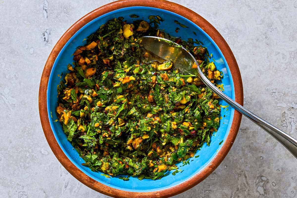 Herb and pistachio salsa in a bowl with a spoon.