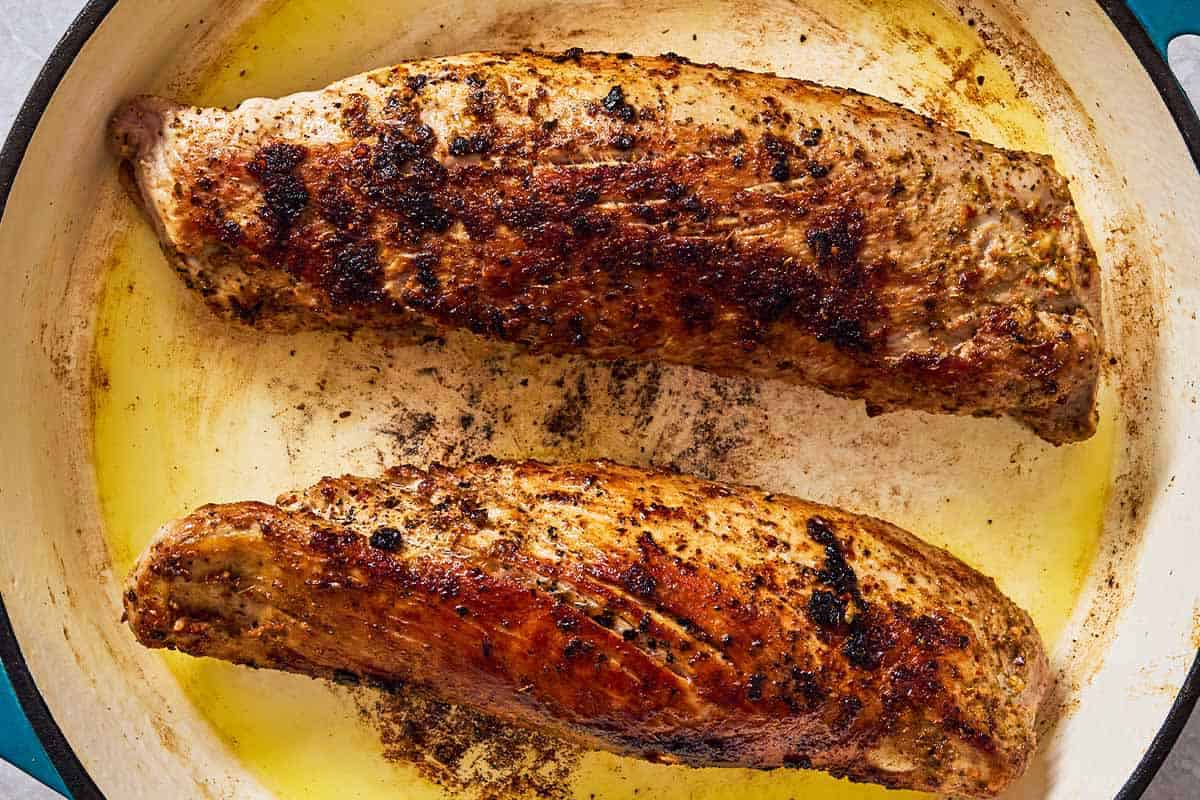 2 pork tenderloins being seared in a skillet.