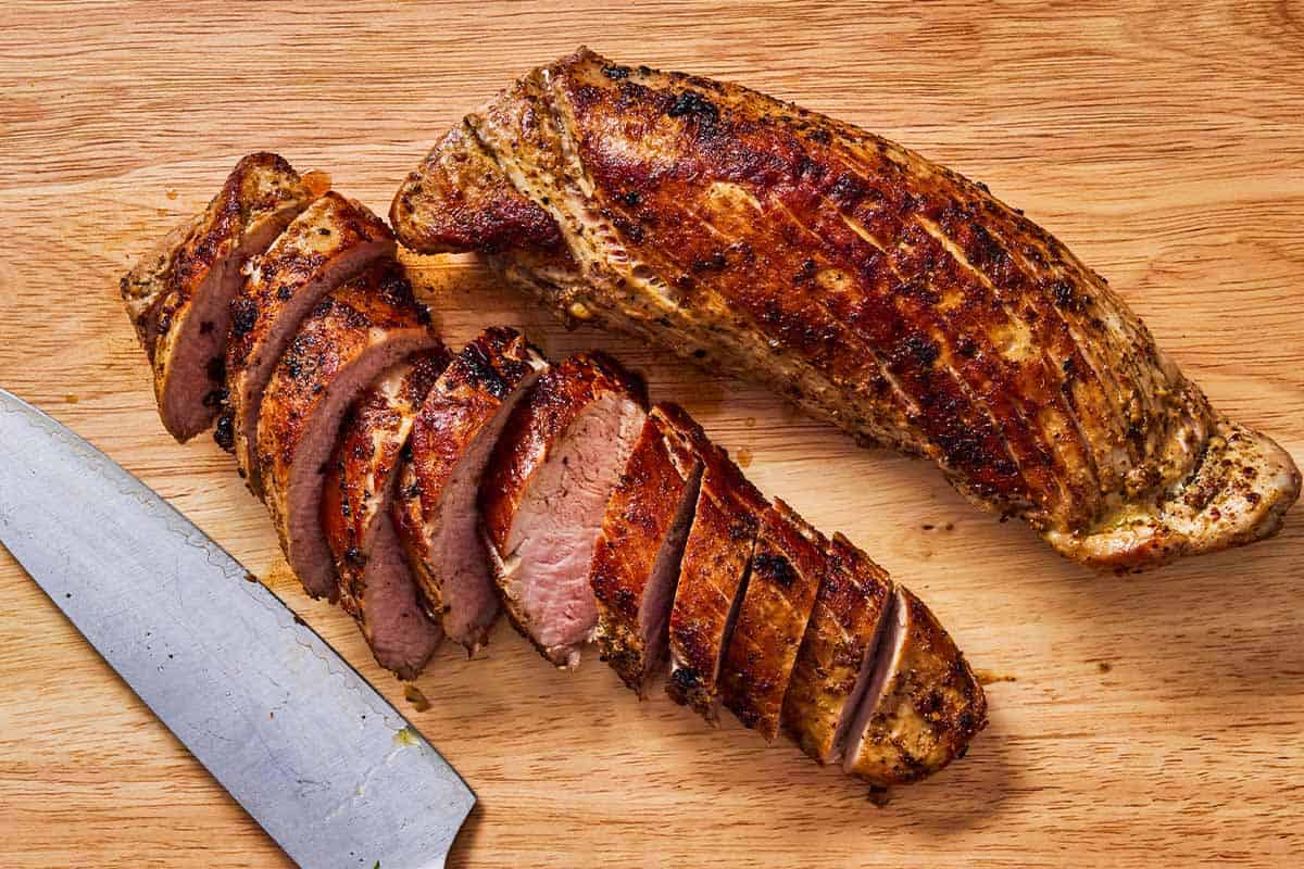 2 baked pork tenderloins on a cutting board with a knife. One is sliced, one is not.