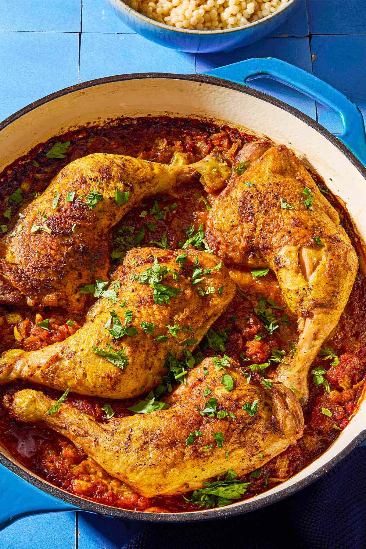 A close up of apricot chicken and apricot sauce garnished with chopped mint and parsley in a skillet.