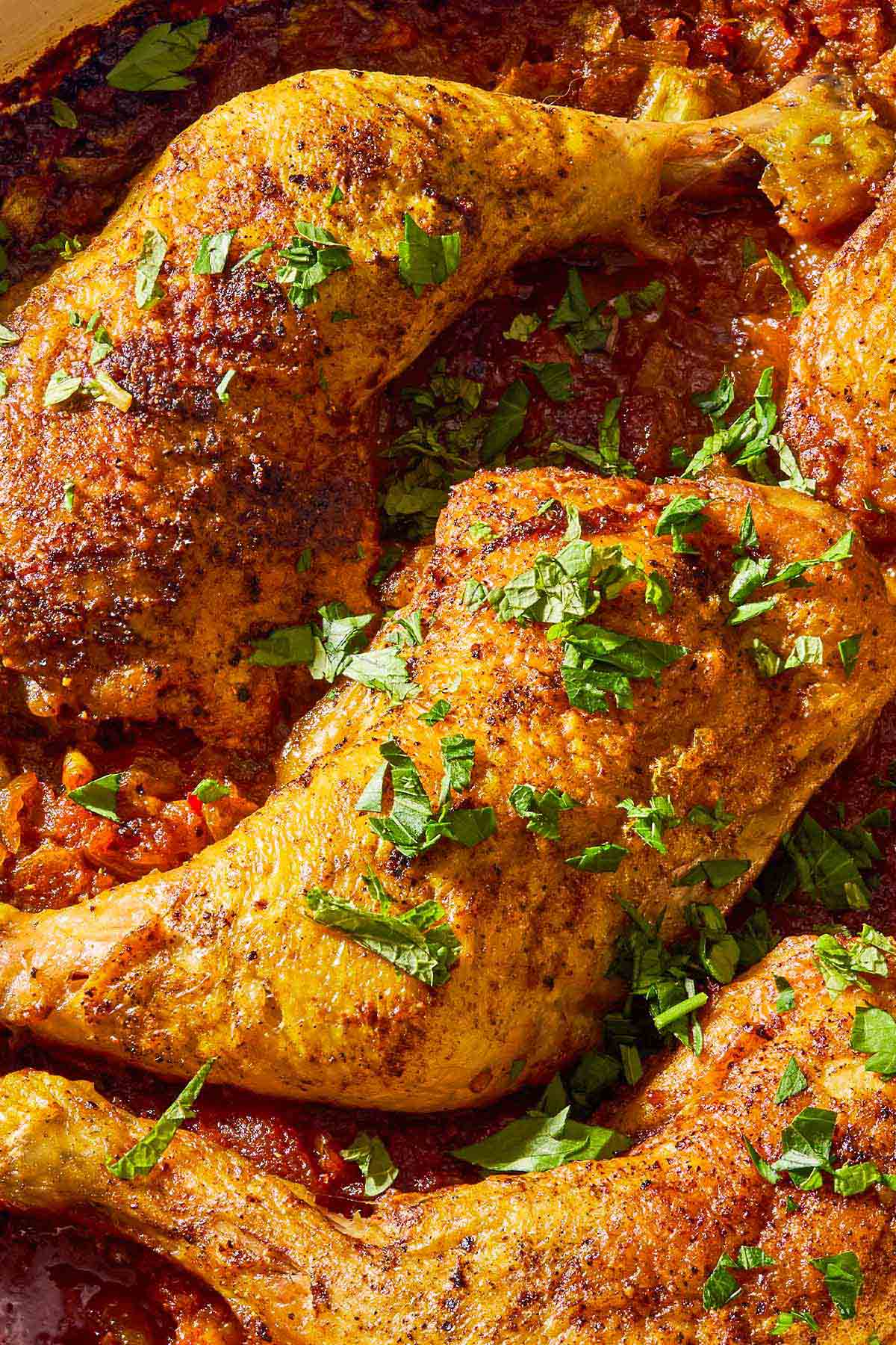 A close up of apricot chicken and apricot sauce garnished with chopped mint and parsley.