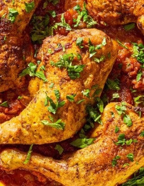 A close up of apricot chicken and apricot sauce garnished with chopped mint and parsley in a skillet.