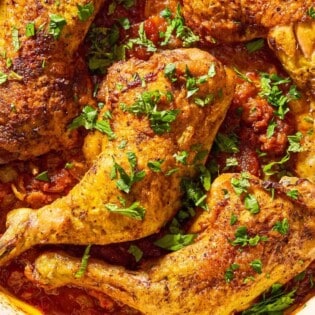 A close up of apricot chicken and apricot sauce garnished with chopped mint and parsley in a skillet.