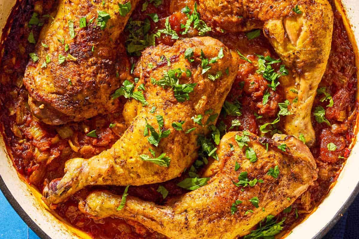 A close up of apricot chicken and apricot sauce garnished with chopped mint and parsley in a skillet.