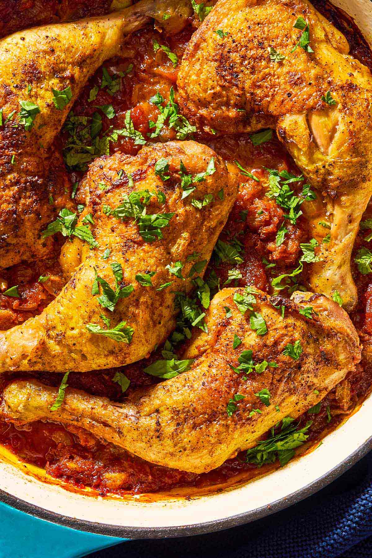 A close up of apricot chicken and apricot sauce garnished with chopped mint and parsley in a skillet.