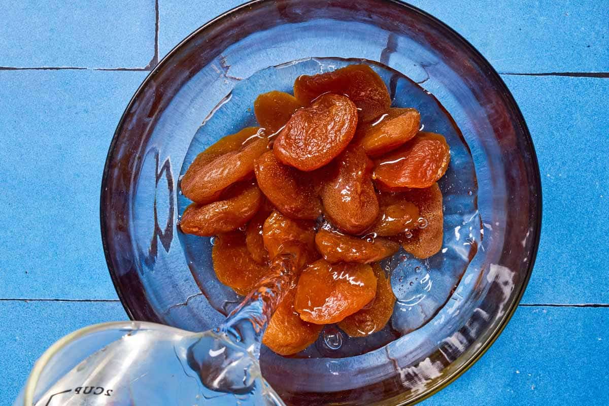 An overhead photo of warm water being poured over dried apricots in a bowl.