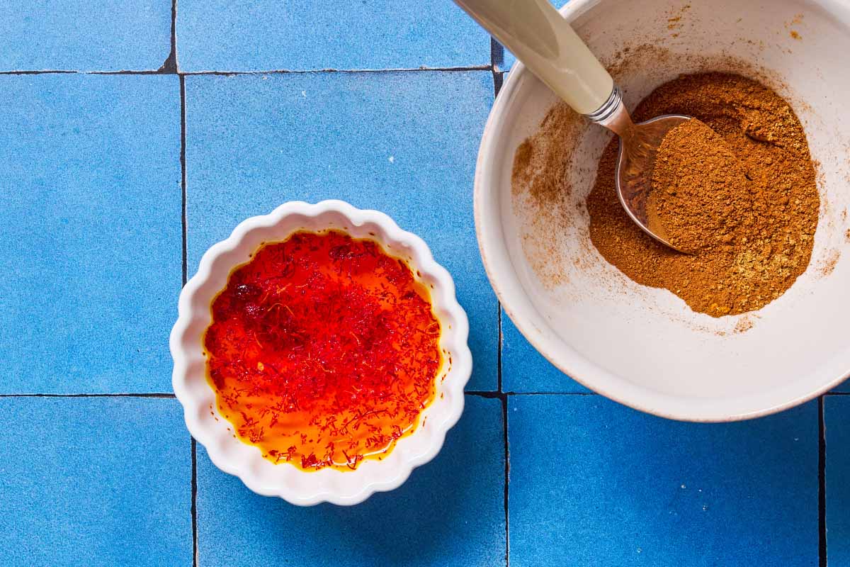 An overhead photo of saffron threads blooming in water next to a bowl of the spice blend with a spoon.