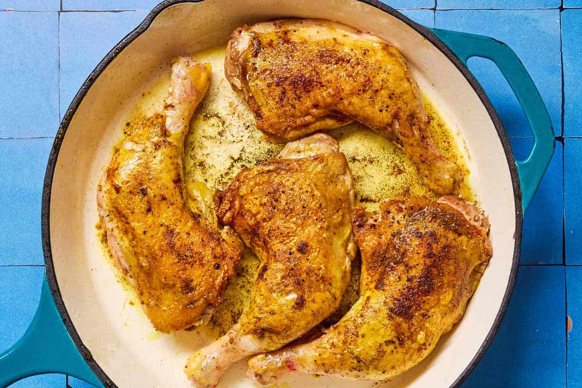 An overhead photo of 4 bone in chicken lets being browned in a skillet.