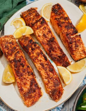 An overhead photo of 4 air fried salmon fillets on a platter with lemon wedges.