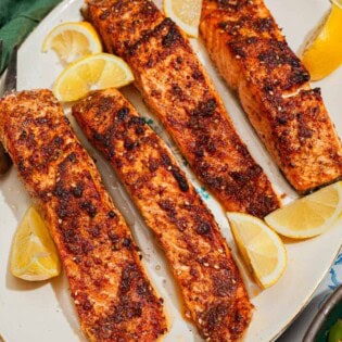 An overhead photo of 4 air fried salmon fillets on a platter with lemon wedges.