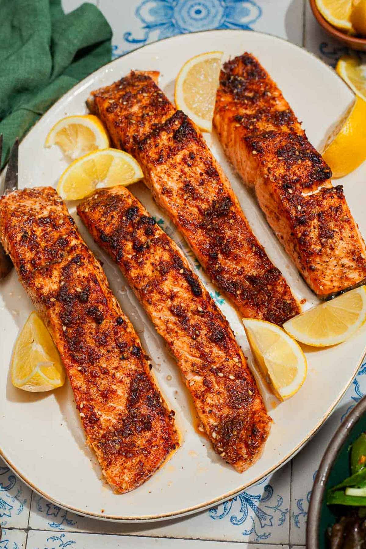 An overhead photo of 4 air fried salmon fillets on a platter with lemon wedges.