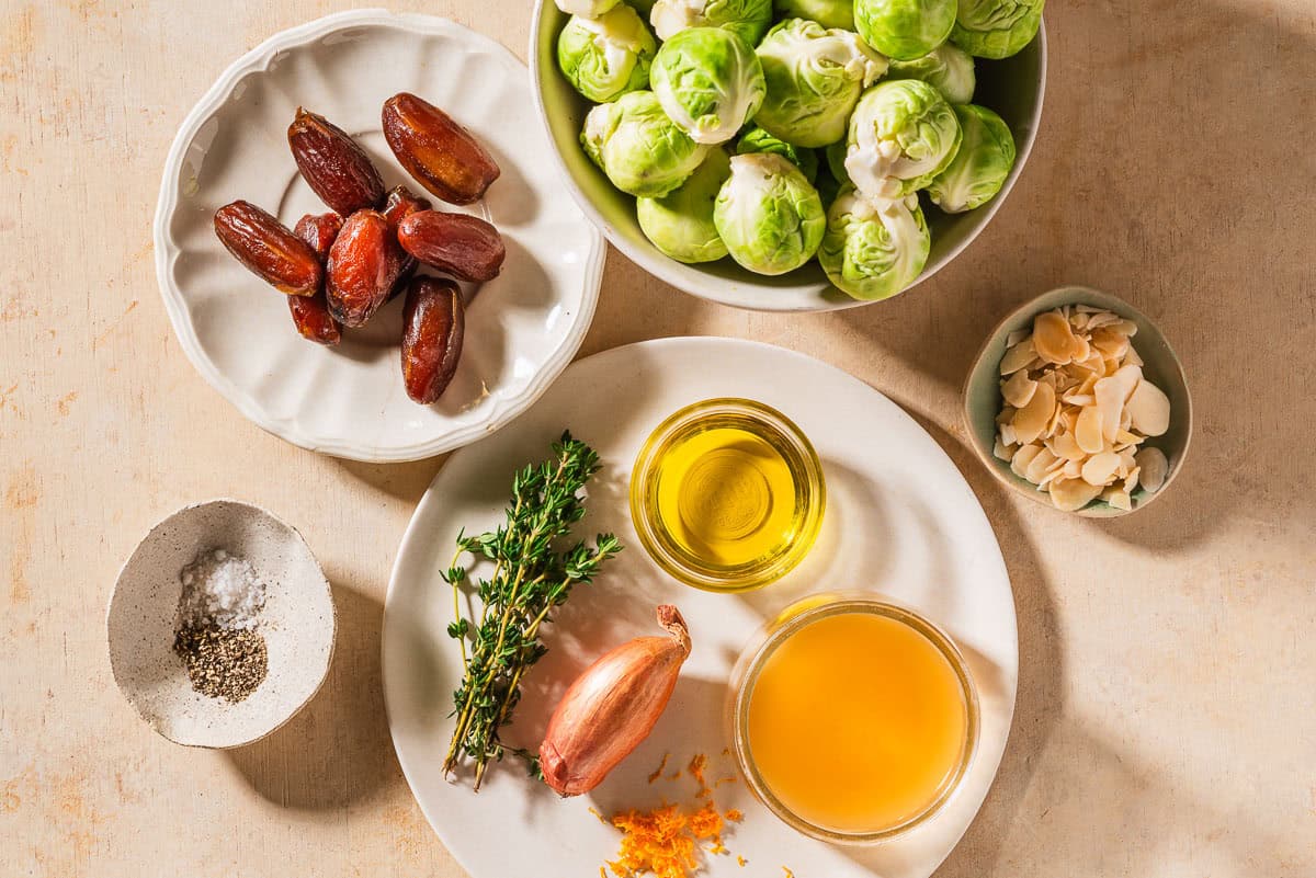 Ingredients for roasted brussels sprouts including brussels sprouts, sliced almonds, olive oil, salt, black pepper, apple cidar vinegar, grated orange zest, fresh thyme, shallot, and dates.