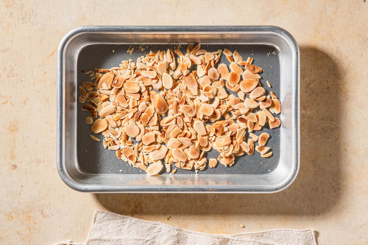 An overhead photo of toasted sliced almonds spread evenly on a baking sheet.